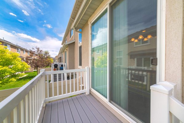 Small deck of a house with sliding glass door and white wood railings. Deck with a view of the neighborhood's yard with lawn and trees.